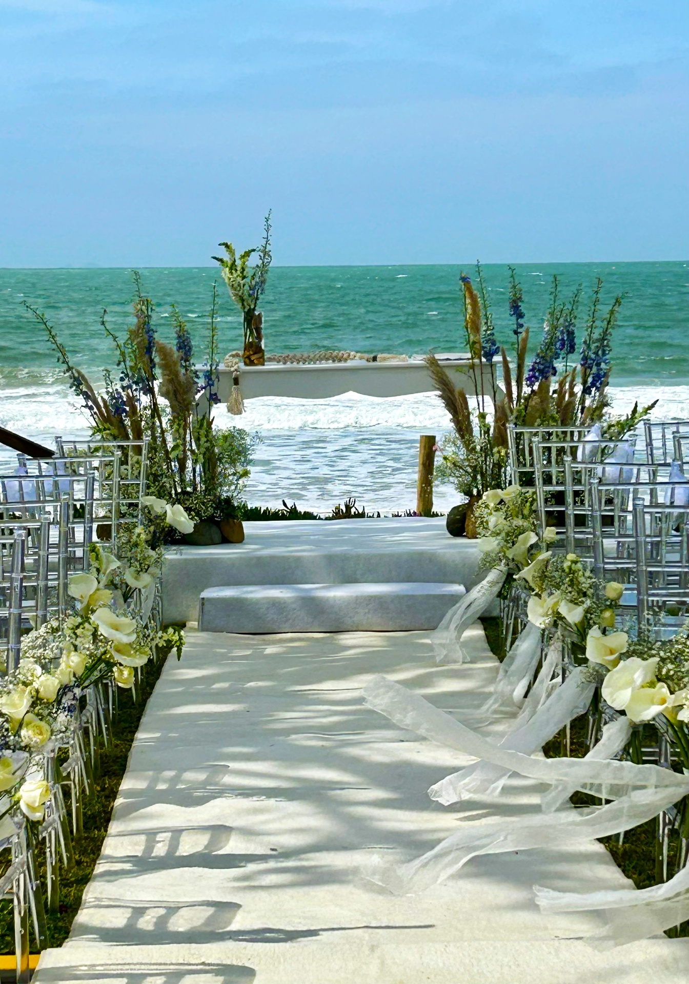 Cerimônia de casamento à beira-mar com altar florido branco e azul, vista para o oceano